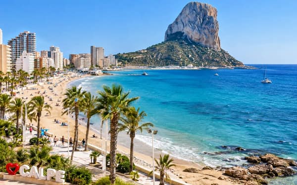 The Arenal-Bol beach and promenade in Calpe, with seafront apartment towers on the left and the Peñón de Ifach rising above the port.
